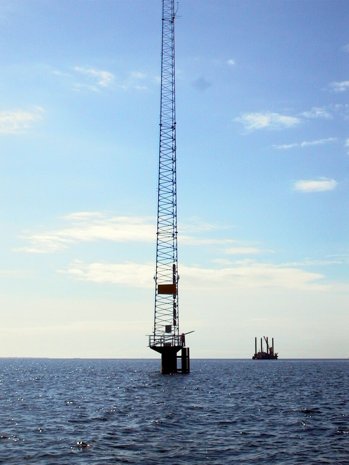 Offshore meteorological mast surrounded by sunlit sea